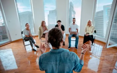 A trainer leading a group session with employees seated in a circle in a bright office