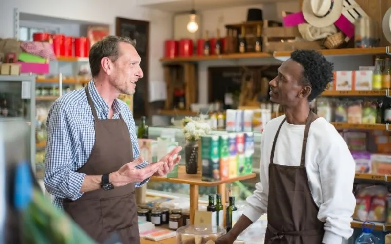 Two shop employees in aprons talking in a grocery store